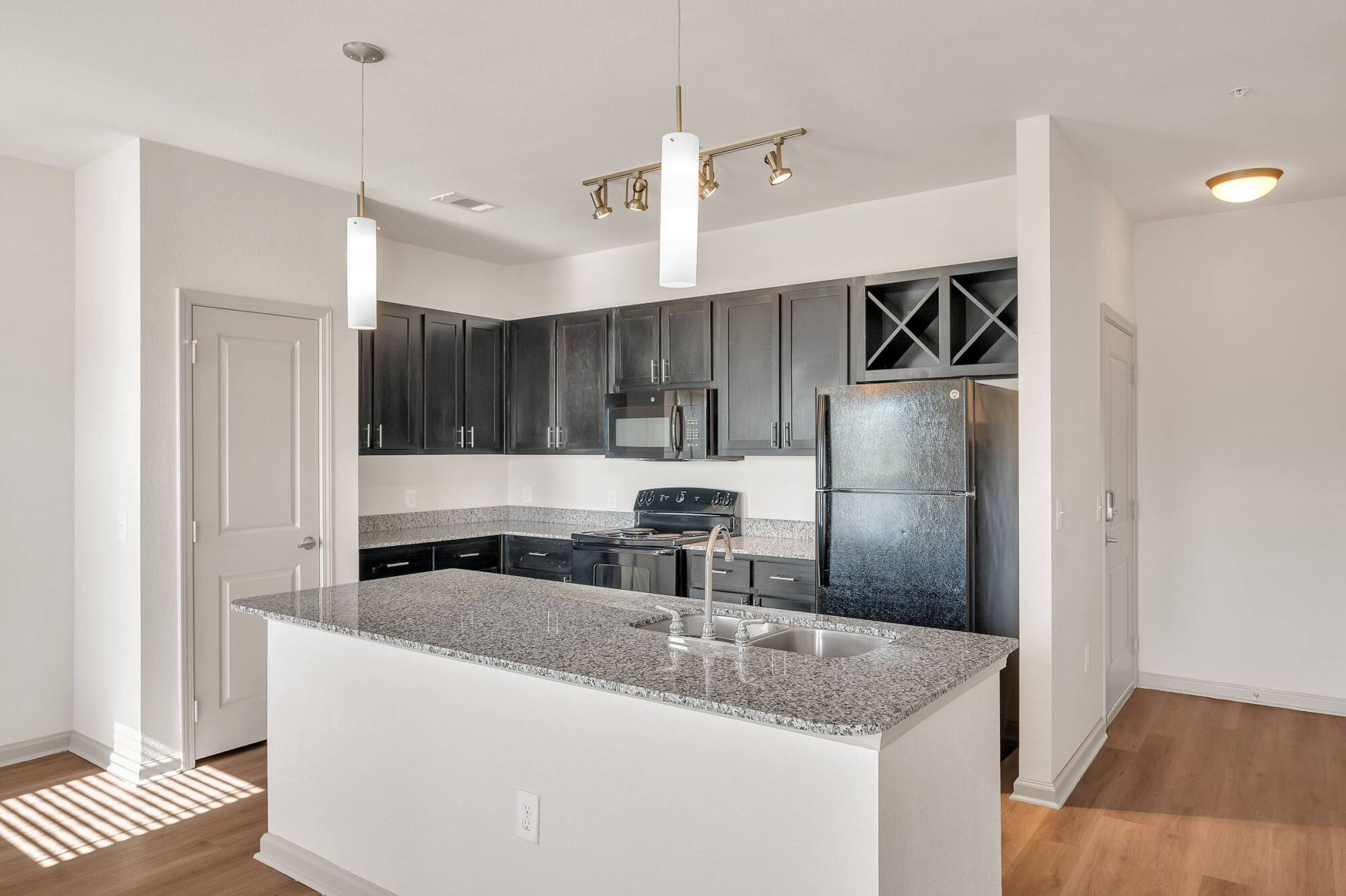 Modern kitchen with dark cabinets, granite countertops, black appliances, and pendant lighting over an island.