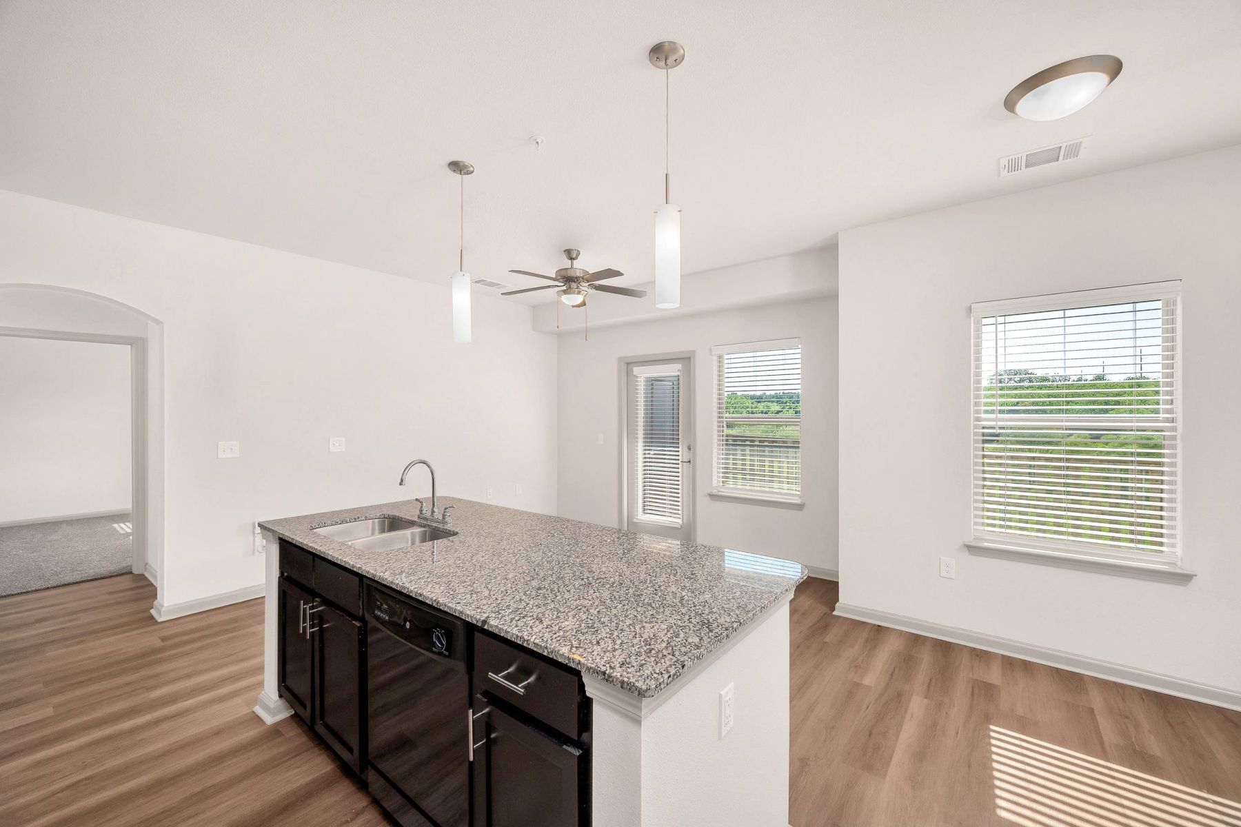 Empty room with wood floors, ceiling fan, and sliding glass door leading to a patio with vertical blinds at Apex West Midown.